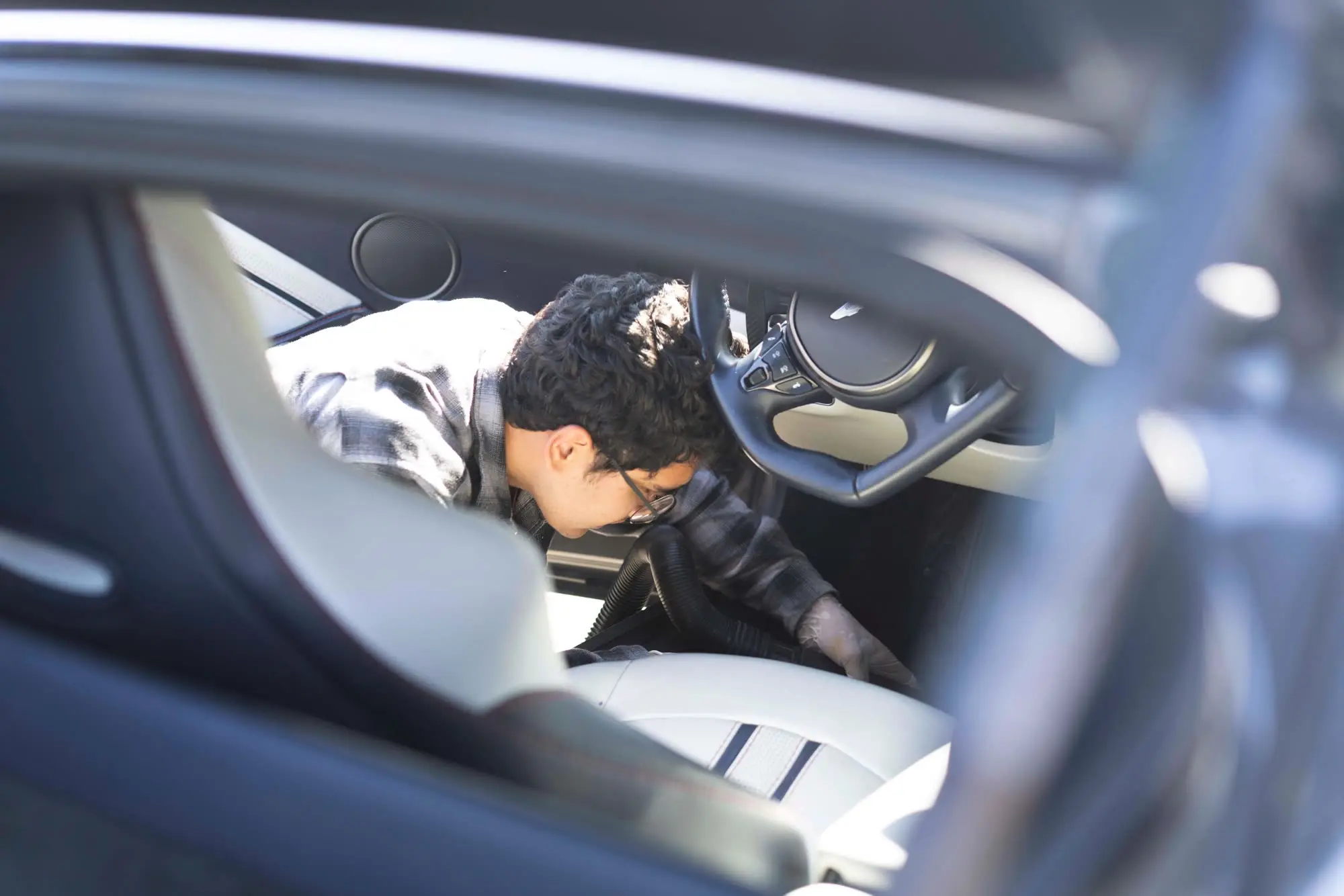 Detailer vacuuming/cleaning Aston Martin Vantage interior, framed through window