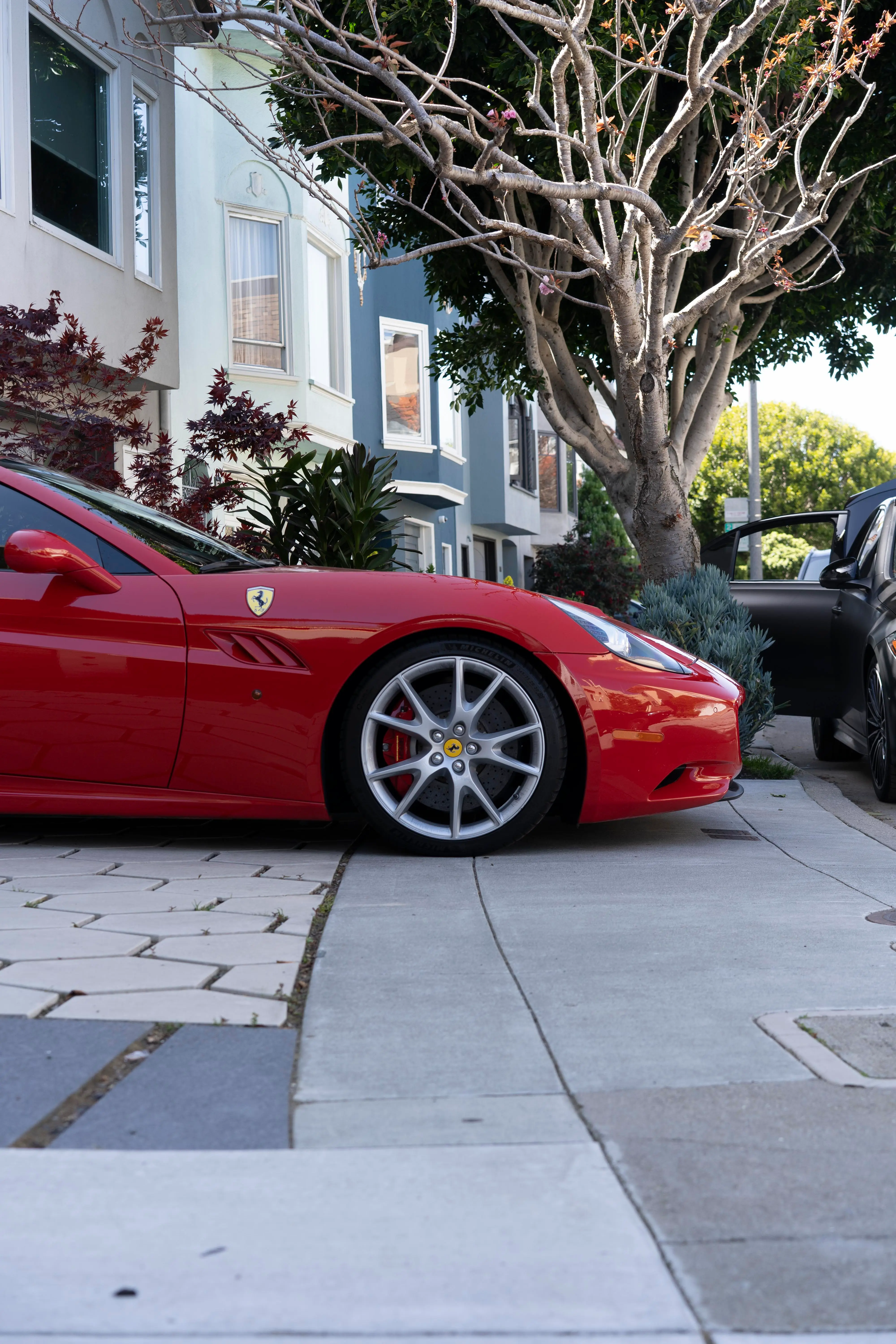 Red Ferrari California on a tree-lined San Francisco sidewalk