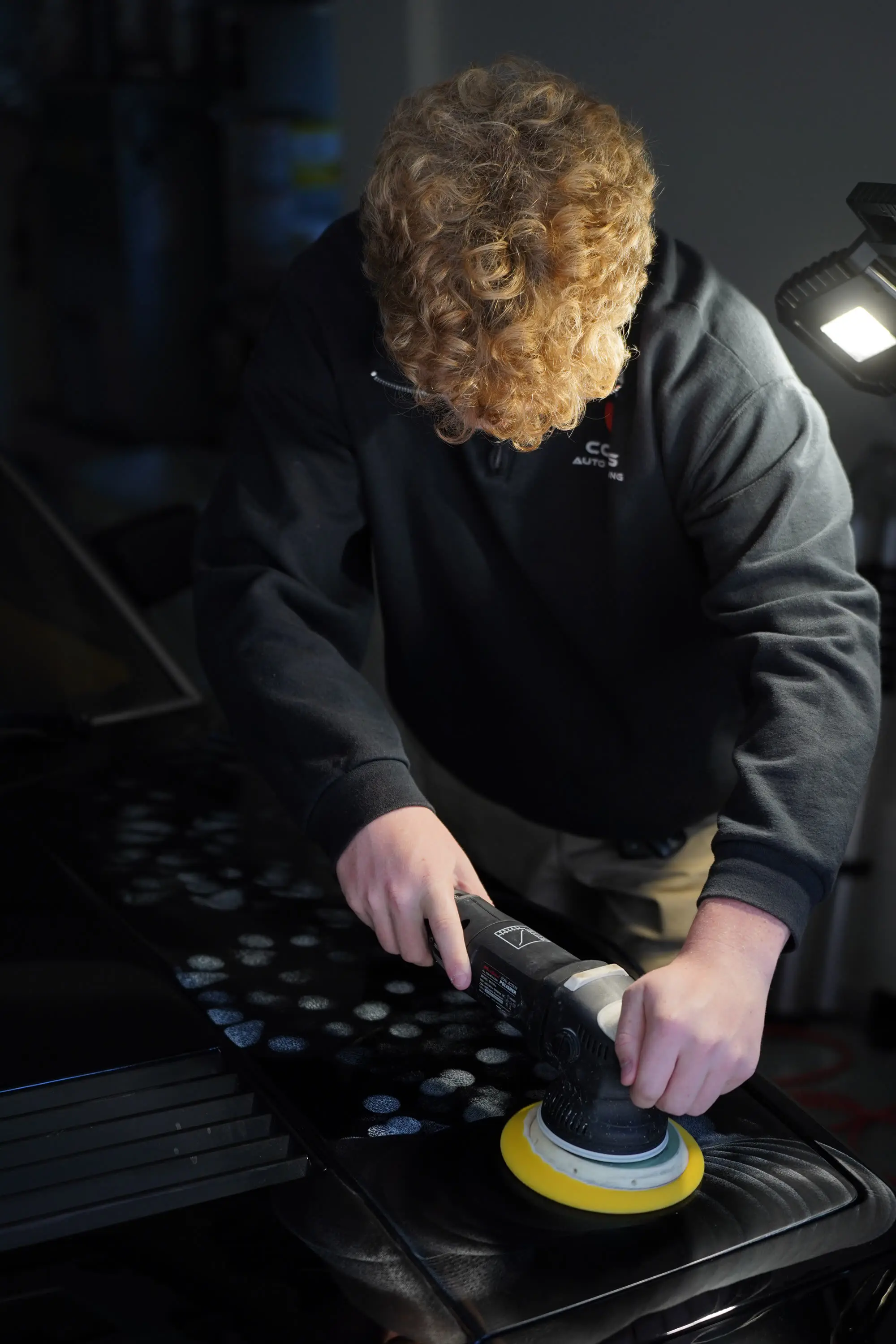 Detailer machine-polishing a black Ferrari 400i hood