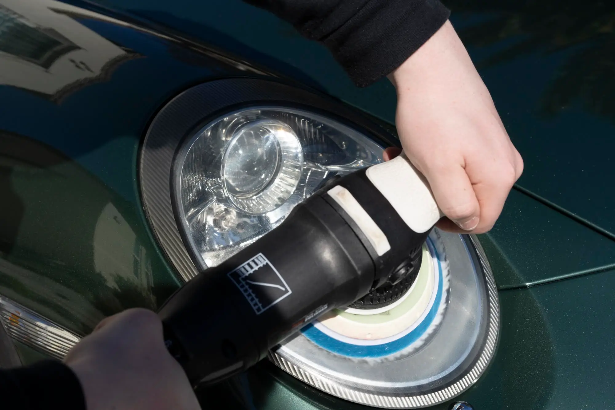 Hands machine-polishing a Porsche 911 headlight